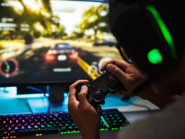 A gamer wearing a headset grips a controller in front of a racing game