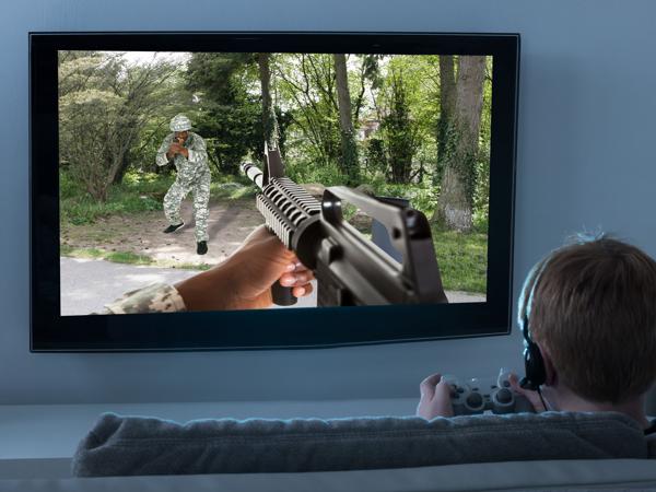 A boy wearing headphones plays a shooting game on a TV with a controller